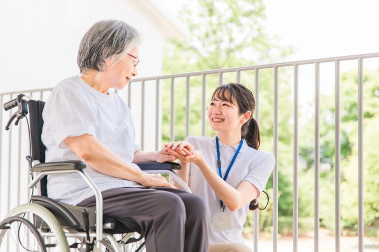 日本人の高齢女性が屋外で笑顔を見せ介護スタッフが寄り添う様子